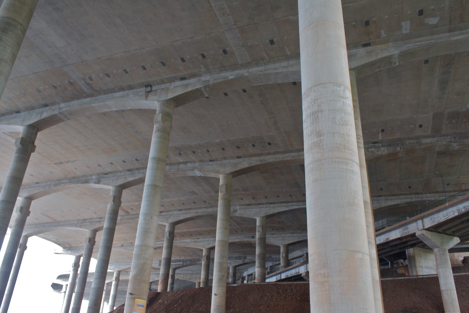 Looking up from ground level into the forest of concrete columns holding Madeira Airport’s runway deck in the air, the underside of the deck filling the top of the frame.