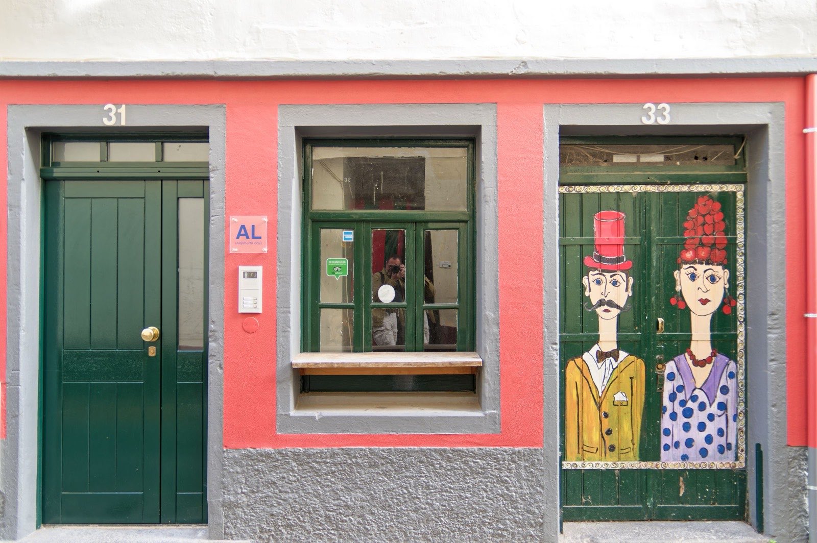 Two doorways on a coral-pink Funchal facade: one plain dark green, the next painted with a couple in a top hat and a red headdress.
